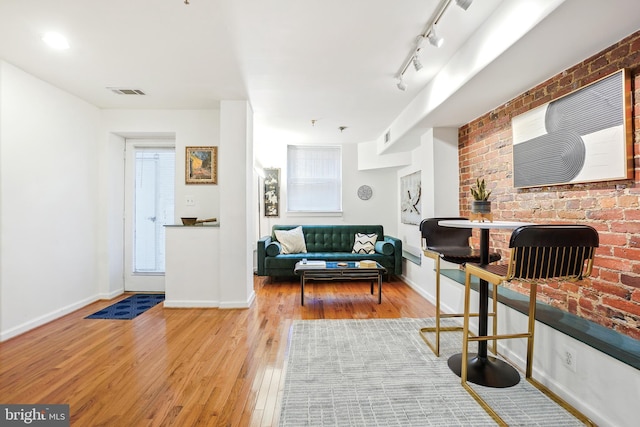 interior space with hardwood / wood-style flooring, track lighting, and brick wall