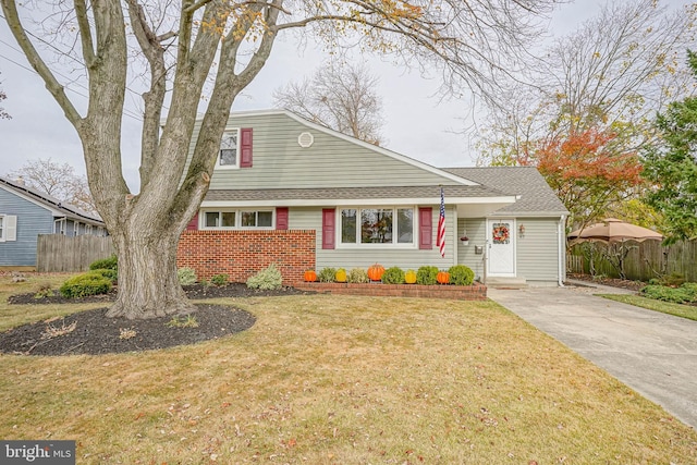 view of front of home featuring a shingled roof, fence, a front lawn, and brick siding