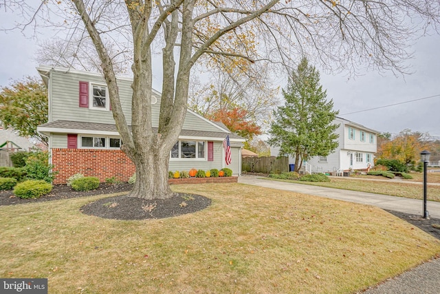 view of front facade featuring brick siding, a shingled roof, fence, driveway, and a front lawn