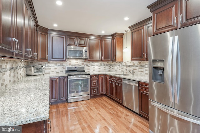 kitchen featuring light stone counters, appliances with stainless steel finishes, a sink, and light wood-style flooring