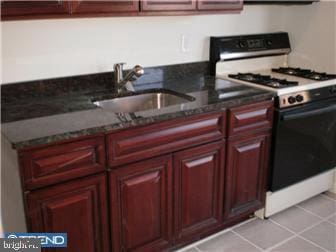 kitchen with sink, light tile patterned floors, dark stone counters, and gas range gas stove