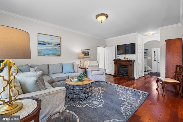 living room featuring arched walkways, ornamental molding, wood-type flooring, and a glass covered fireplace