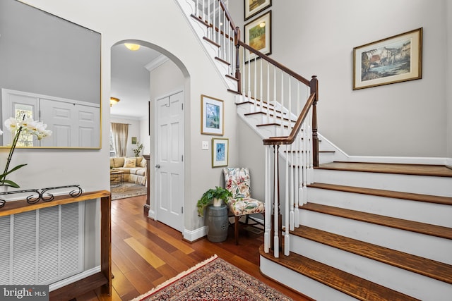 staircase with arched walkways, baseboards, hardwood / wood-style flooring, and crown molding