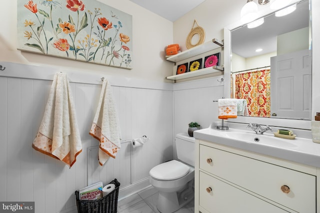 full bathroom with toilet, marble finish floor, vanity, and wainscoting