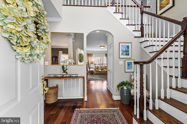 entrance foyer featuring baseboards, visible vents, arched walkways, hardwood / wood-style floors, and a high ceiling