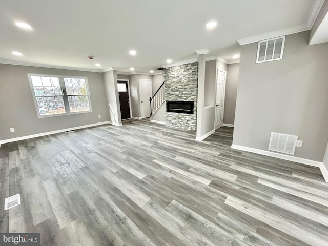 unfurnished living room featuring a stone fireplace, ornamental molding, and light wood-type flooring