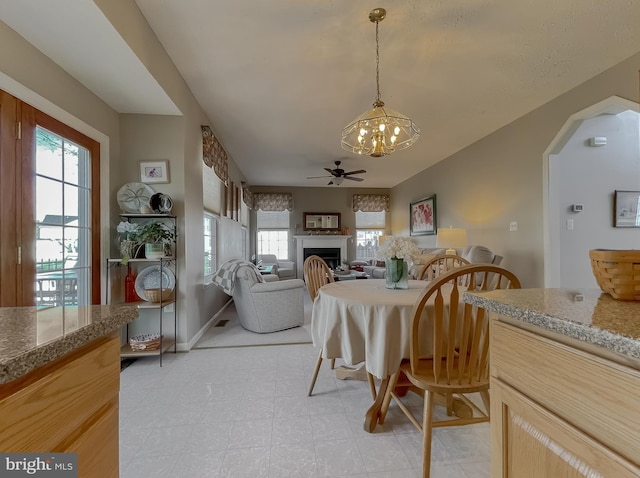 dining room with a fireplace, baseboards, and ceiling fan with notable chandelier