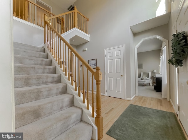 stairs with a towering ceiling, baseboards, and wood finished floors