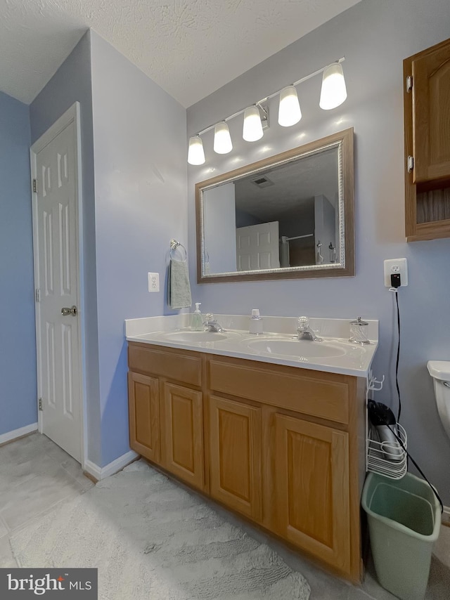 bathroom with a sink, a textured ceiling, toilet, and double vanity