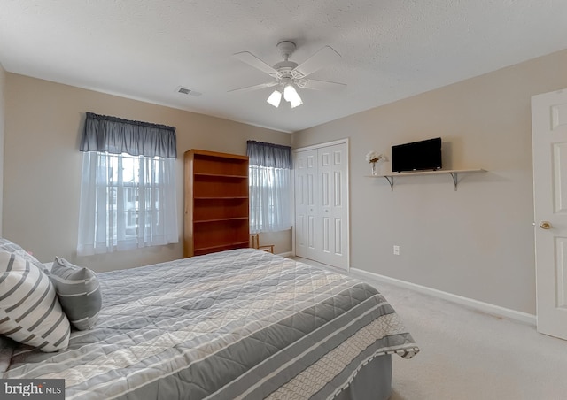 carpeted bedroom with a textured ceiling, ceiling fan, visible vents, baseboards, and a closet