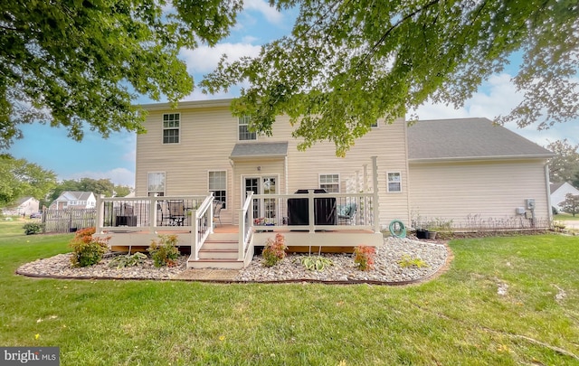 back of property featuring a deck, roof with shingles, and a lawn