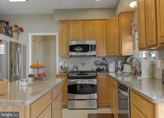 kitchen with light tile patterned floors, decorative backsplash, appliances with stainless steel finishes, light stone countertops, and a sink