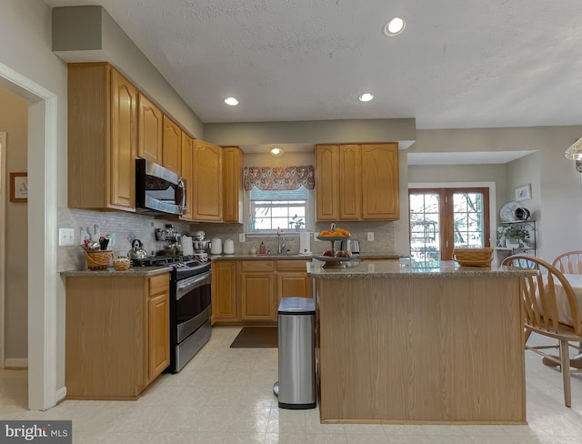 kitchen with a sink, appliances with stainless steel finishes, a center island, light floors, and tasteful backsplash