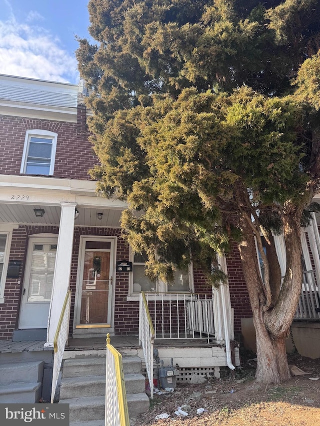 doorway to property featuring covered porch and brick siding