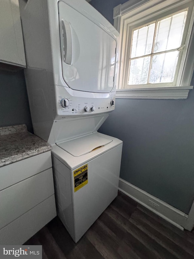 washroom featuring stacked washer and dryer, cabinet space, baseboards, and dark wood-style floors