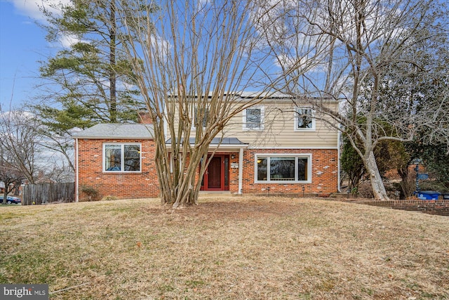 traditional-style house featuring a chimney, fence, a front lawn, and brick siding