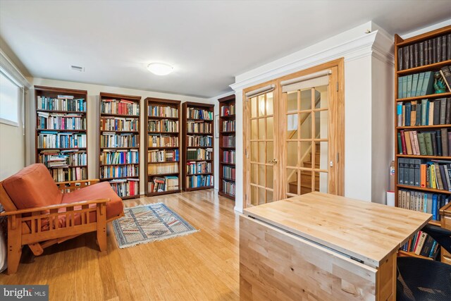 sitting room with wall of books, light wood-style floors, and visible vents