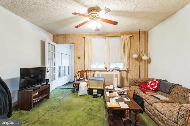 living room with ceiling fan, wood walls, a textured ceiling, and dark colored carpet