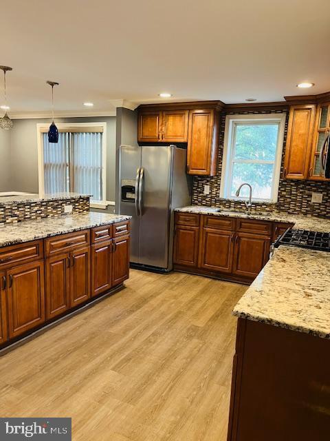 kitchen with stainless steel fridge, decorative backsplash, hanging light fixtures, range, and light wood-type flooring