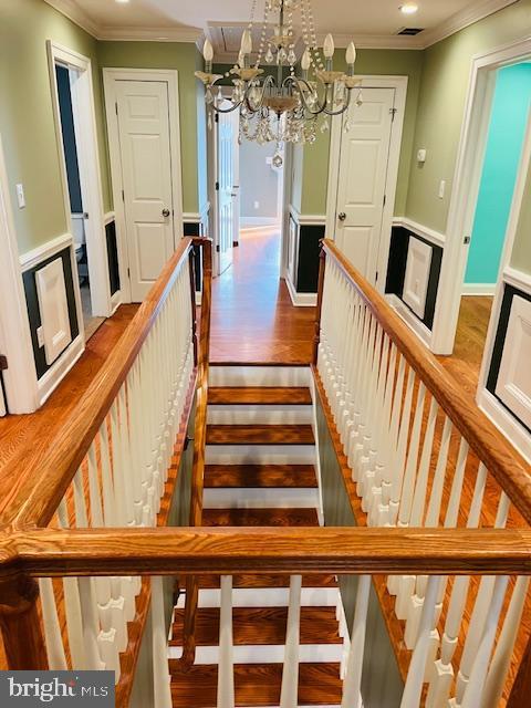 staircase featuring wood-type flooring, crown molding, and an inviting chandelier