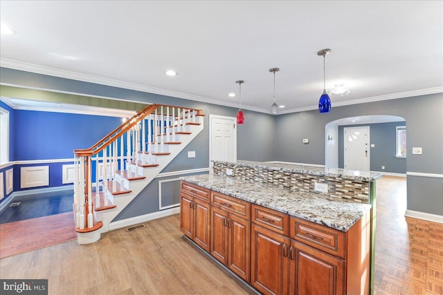 kitchen featuring pendant lighting, ornamental molding, a center island, and light stone counters