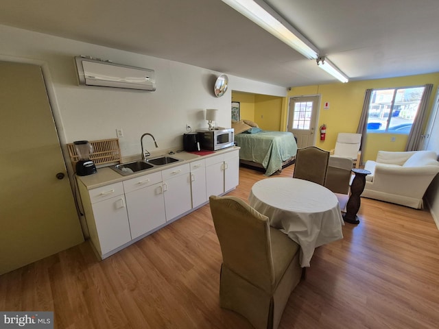 kitchen featuring an AC wall unit, sink, light hardwood / wood-style flooring, and white cabinets