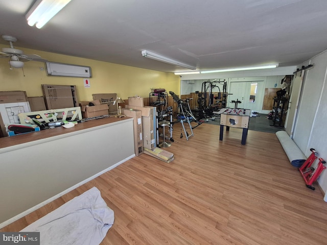 interior space featuring ceiling fan, a barn door, a wall mounted AC, and light hardwood / wood-style floors