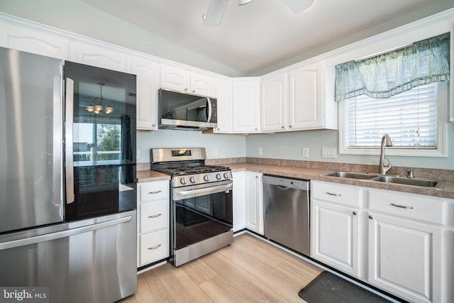 kitchen with lofted ceiling, sink, appliances with stainless steel finishes, white cabinetry, and light hardwood / wood-style floors