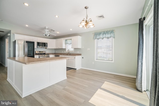 kitchen with a kitchen island, appliances with stainless steel finishes, sink, white cabinets, and hanging light fixtures