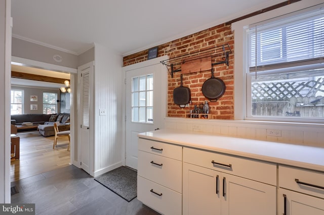 kitchen featuring white cabinets, brick wall, ornamental molding, and light countertops