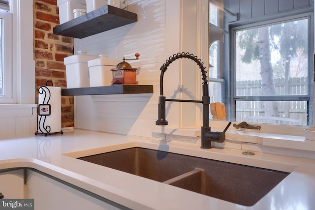 kitchen featuring brick wall, light countertops, and a sink