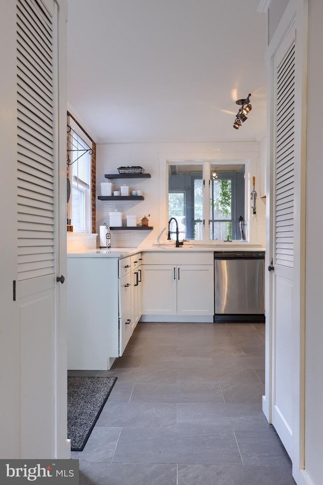 kitchen with light countertops, stainless steel dishwasher, white cabinetry, open shelves, and a sink