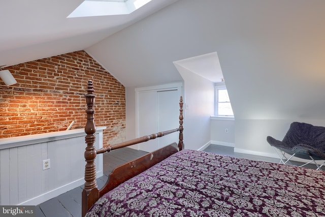 bedroom with brick wall, vaulted ceiling with skylight, baseboards, and a wainscoted wall