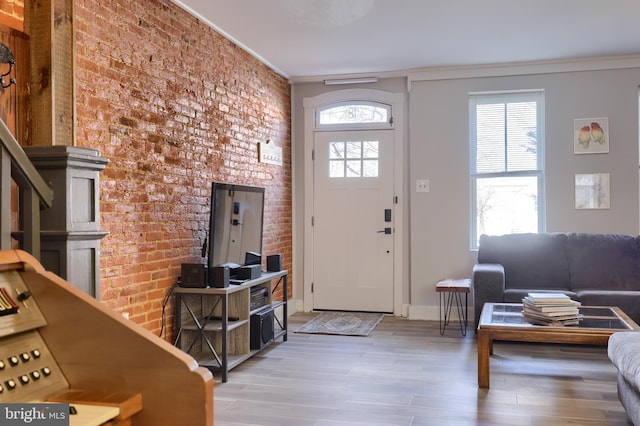 entryway featuring light wood finished floors, brick wall, baseboards, and ornamental molding