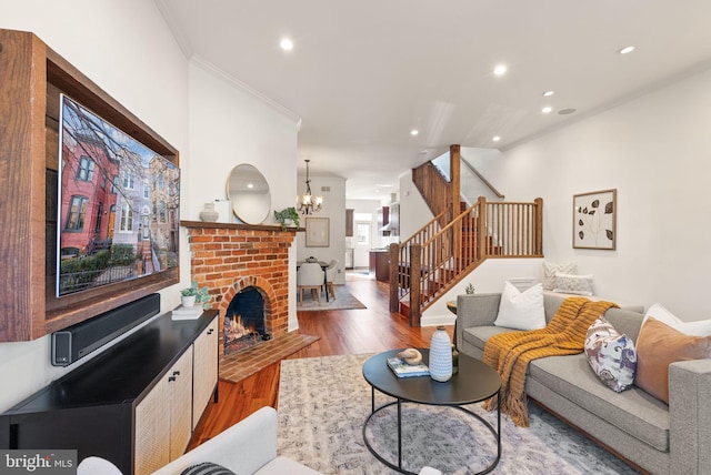 living room with crown molding, a notable chandelier, hardwood / wood-style flooring, and a brick fireplace