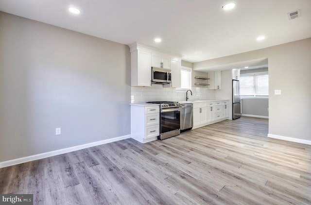 kitchen with sink, tasteful backsplash, light wood-type flooring, stainless steel appliances, and white cabinets