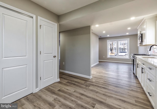 kitchen featuring light stone counters, appliances with stainless steel finishes, light hardwood / wood-style floors, and white cabinets