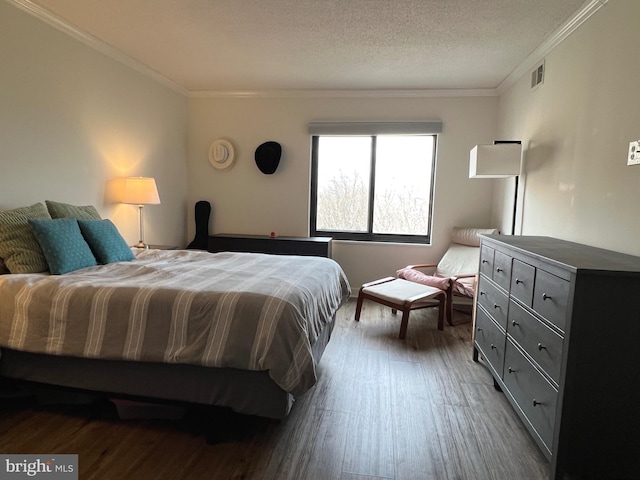 bedroom with visible vents, a textured ceiling, ornamental molding, and wood finished floors