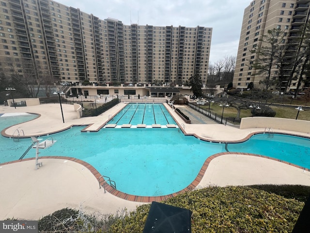 community pool featuring a patio area, fence, and a city view