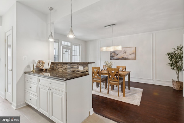 kitchen with white cabinetry, dark stone countertops, decorative backsplash, decorative light fixtures, and light wood-type flooring