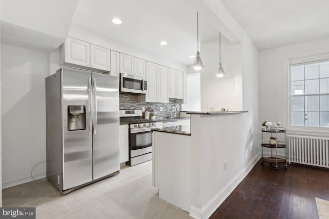 kitchen featuring sink, decorative light fixtures, appliances with stainless steel finishes, radiator heating unit, and white cabinets