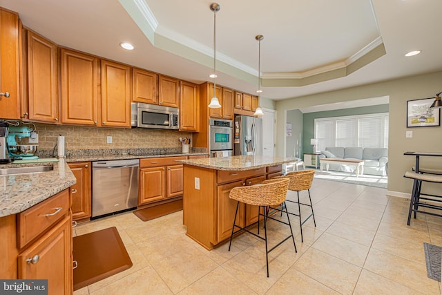 kitchen featuring pendant lighting, a kitchen breakfast bar, stainless steel appliances, a center island, and a raised ceiling