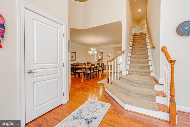 stairs featuring ornamental molding, hardwood / wood-style floors, and an inviting chandelier