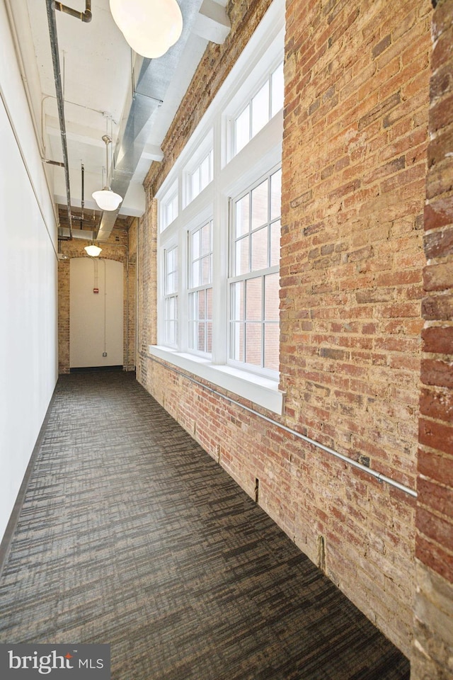 hallway featuring dark carpet and brick wall