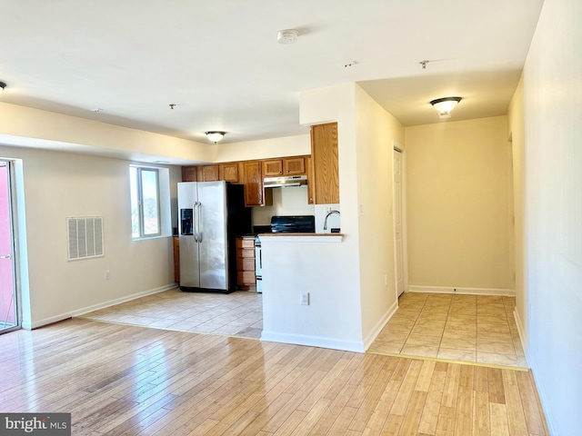 kitchen featuring visible vents, under cabinet range hood, electric stove, brown cabinetry, and stainless steel fridge