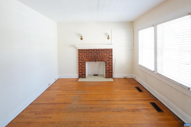 unfurnished living room with wood-type flooring and a brick fireplace