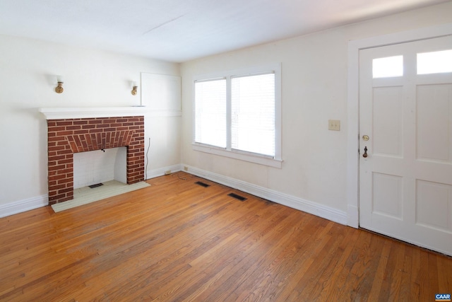 unfurnished living room featuring a brick fireplace and light hardwood / wood-style floors