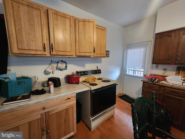 kitchen with vaulted ceiling, light hardwood / wood-style floors, electric range oven, and backsplash