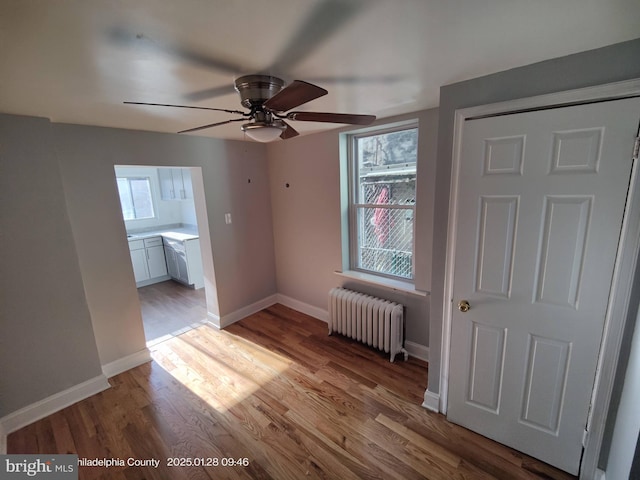 unfurnished bedroom featuring ceiling fan, radiator heating unit, ensuite bath, and light hardwood / wood-style flooring