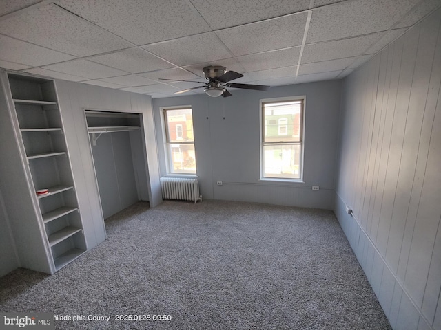 unfurnished bedroom featuring radiator, wooden walls, carpet flooring, a drop ceiling, and a closet